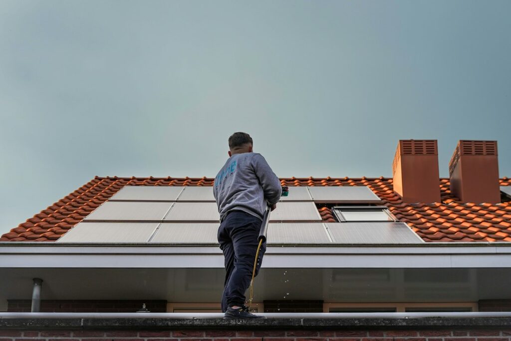 Homeowner checks a residential roof from the ground while a secured ladder rests beside the house.